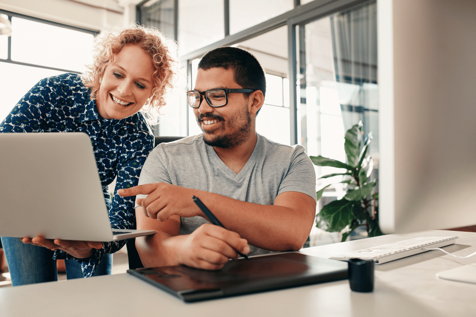 two people looking at a laptop and using computers in a work setting