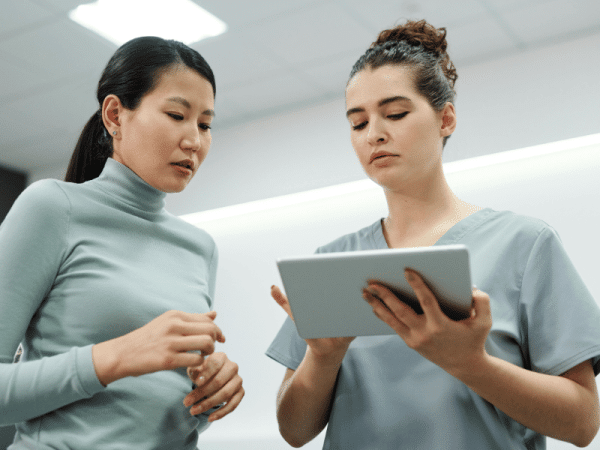 Alt text: Healthcare professional reviewing information on a tablet with a colleague in a clinical setting.