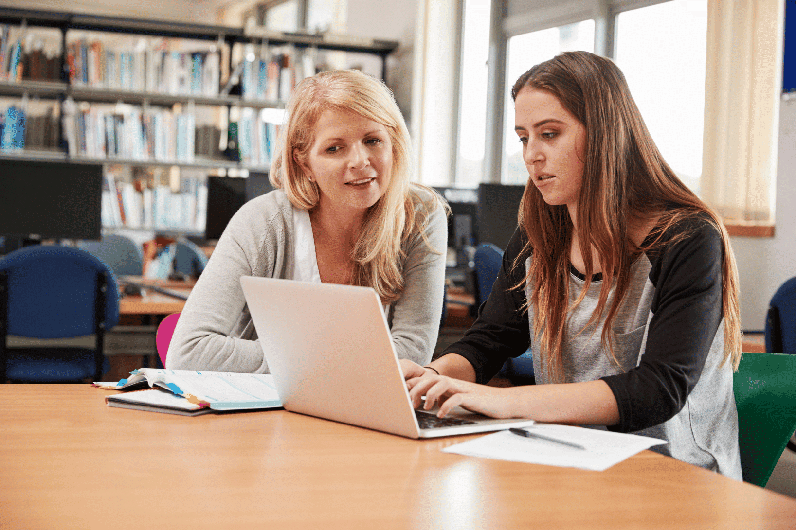 A teacher and a student reviewing study data together on a laptop in an academic setting.